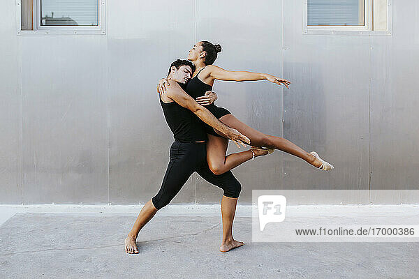 Junge männliche und weibliche professionelle Akrobaten umarmen sich beim Tanzen gegen die Wand
