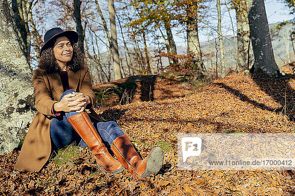 Smiling woman sitting under tree in forest