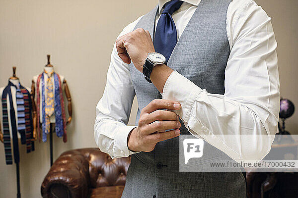 Man in gray waistcoat fastening shirt cuff in tailors boutique
