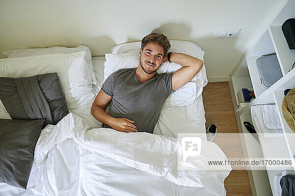 Smiling man with hand behind head resting in bedroom