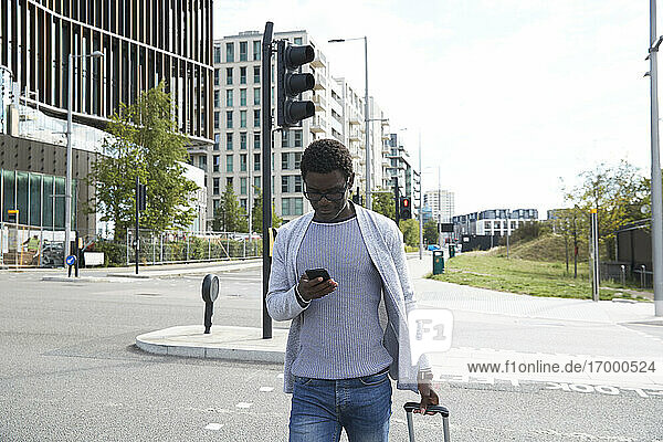 Männlicher Unternehmer  der ein Mobiltelefon benutzt  während er in der Stadt auf der Straße geht