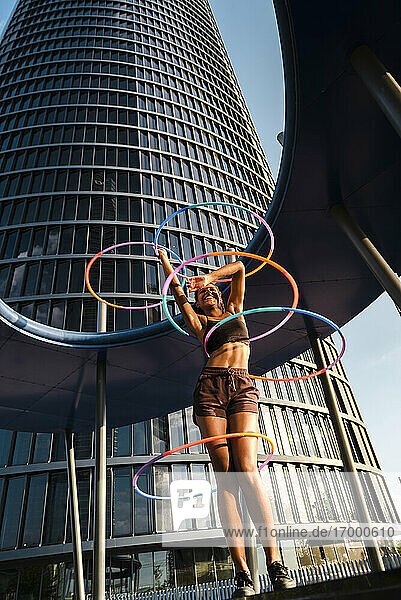 Fröhliche sportliche Frau  die mit Plastikreifen vor einem modernen Bürogebäude trainiert