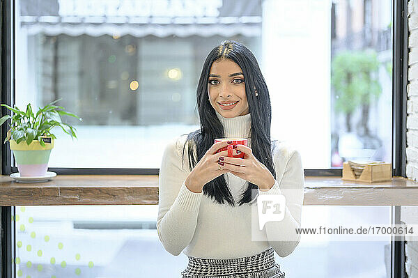 Lächelnde Geschäftsfrau  die eine Tasse Kaffee gegen das Fenster eines Cafés hält