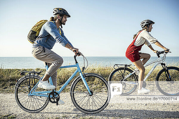 Couple wearing helmet riding bicycles against sea