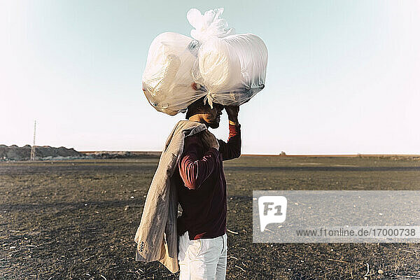 Junger Mann trägt eine Tasche mit Plastikflaschen auf dem Kopf in einem kargen Land