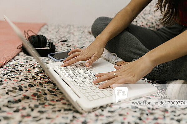Teenager-Mädchen probiert einen Laptop aus  während sie auf dem Bett sitzt