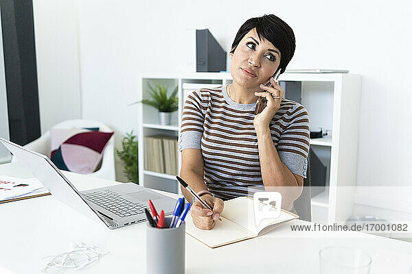 Porträt einer Geschäftsfrau  die am Schreibtisch mit einem Smartphone telefoniert