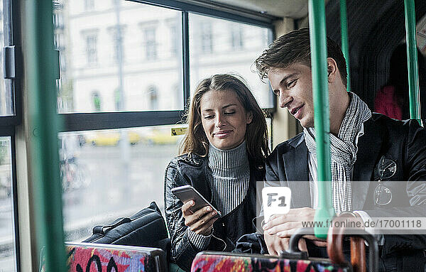 Smiling female and male colleagues using smart phone while commuting through bus