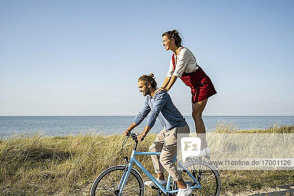 Smiling woman enjoying ride with man while standing on bicycle against clear sky
