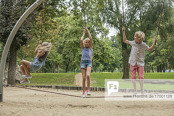 Glücklicher Junge und Mädchen hängen an einem Seil auf einem Spielplatz im Park