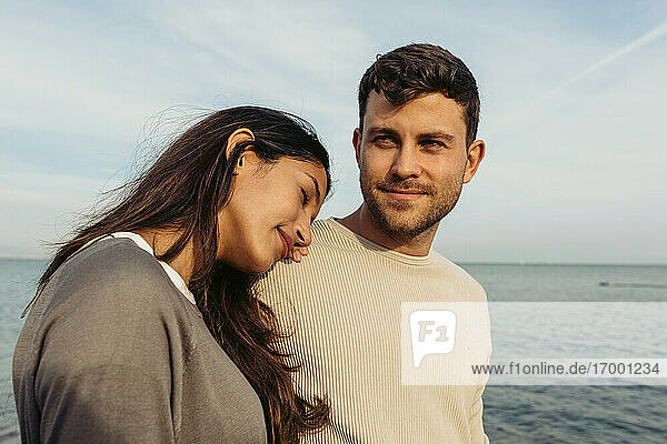 Young woman leaning on man's shoulder against sky at beach