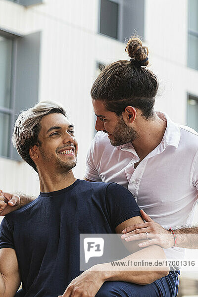 Smiling man looking at gay partner against building in city