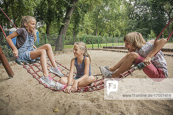 Fröhlicher Junge und Mädchen spielen auf einer Seilschaukel auf einem Spielplatz
