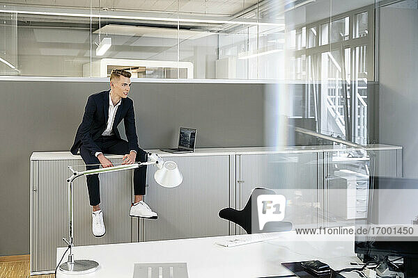 Young businessman wearing suit looking away while sitting on table at office