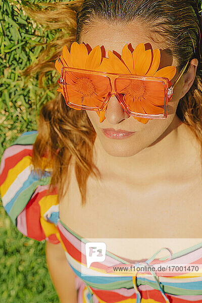 Porträt einer auf einer Wiese liegenden Frau mit Brille und orangefarbenen Blumen  die ihre Augen bedecken