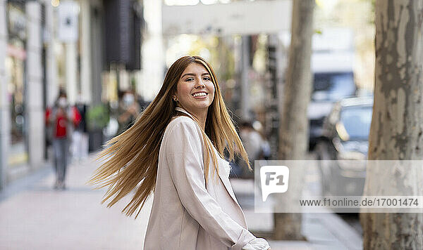 Smiling woman spinning while standing on footpath in city