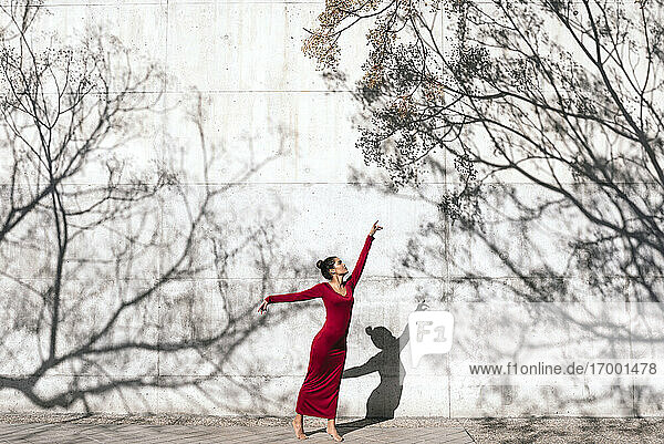 Woman in red dress with dancer pose and tree shadows on wall