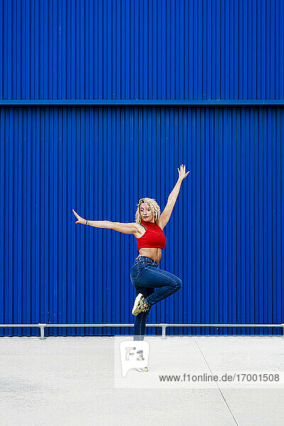 Junge Frau tanzt vor einer blauen Wand in der Stadt