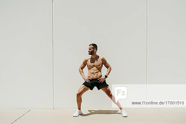 Barechested male athlete stretching in sunshine