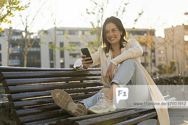 Glückliche Geschäftsfrau  die ihr Smartphone hält und auf einer Bank sitzt