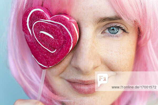 Porträt einer jungen Frau mit rosa Perücke und herzförmigem Lolli  der ihr Auge bedeckt