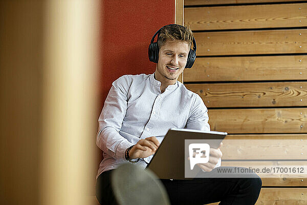 Mann mit Kopfhörern  der ein digitales Tablet benutzt  während er zu Hause sitzt