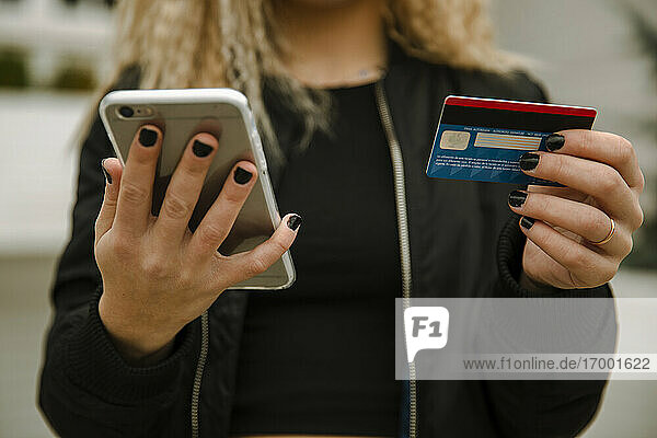 Junge Frau beim Einkaufen mit Smartphone und Kreditkarte