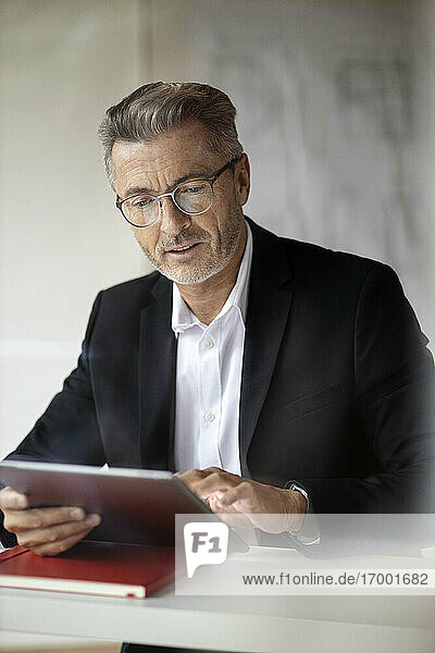 Geschäftsmann mit Brille  der bei der Arbeit zu Hause ein digitales Tablet benutzt