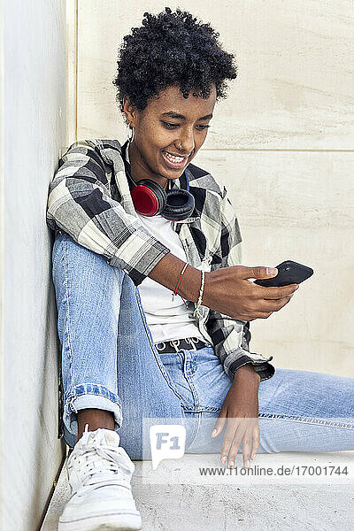 Schöner junger weiblicher Hipster  der sein Smartphone benutzt  während er an einer Stützmauer sitzt
