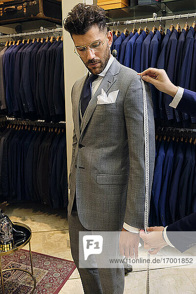 Tailor in his menswear store taking customers measurements for suit