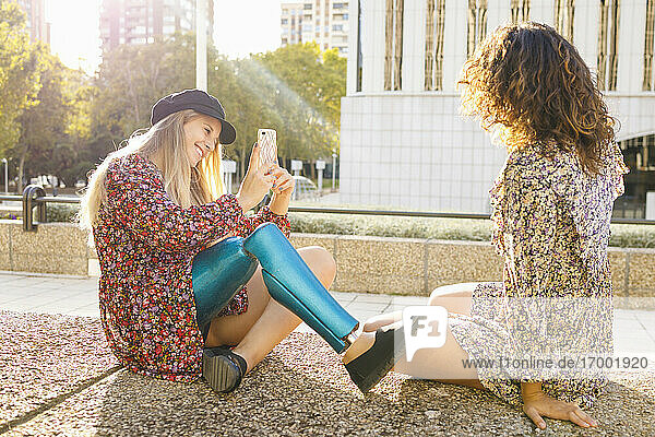 Lächelnde behinderte Frau  die ihre Freundin auf dem Fußweg sitzend an einem sonnigen Tag fotografiert