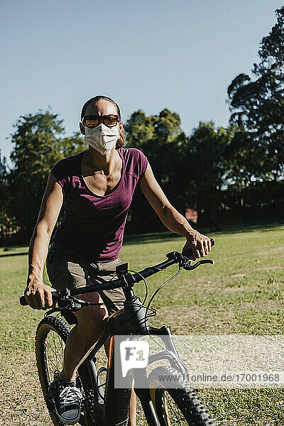 Frau mit Gesichtsmaske fährt mit einem elektrischen Mountainbike im Park