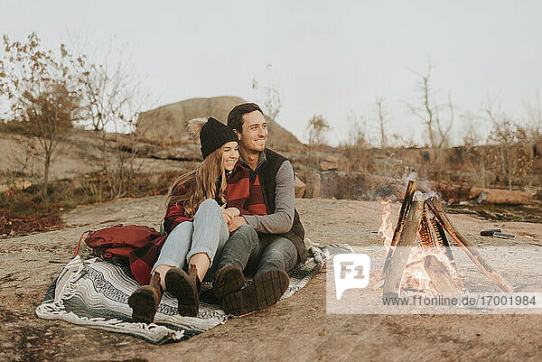 Young couple sitting together in front of campfire