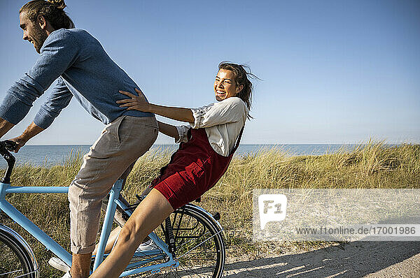 Happy woman enjoying bicycle ride with man against clear sky