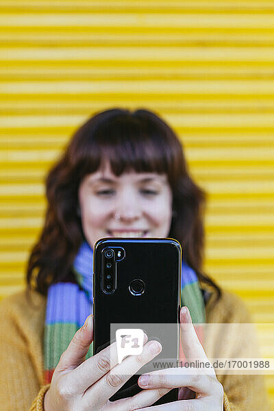 Young woman taking selfie on smart phone against yellow shutter