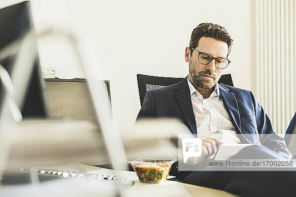 Geschäftsmann  der ein Mobiltelefon benutzt  während er im Büro beim Mittagessen sitzt