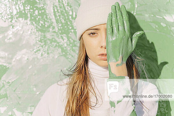 Junge Frau steht vor einem Gemälde und bedeckt ihre Augen mit einer grünen Hand