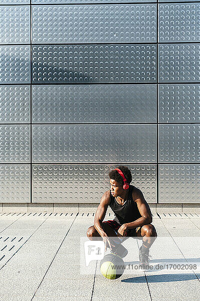Junger Mann mit Kopfhörern und Basketball vor einer metallisch glänzenden Wand