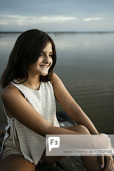 Lächelndes Mädchen sitzt auf einem Steg am See