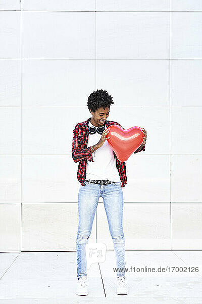 Happy Afro Frau Blick auf rote Herzform Ballon gegen weiße Wand