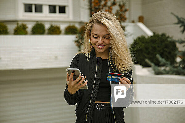 Lächelnde blonde Frau  die mit Mobiltelefon und Kreditkarte online einkauft