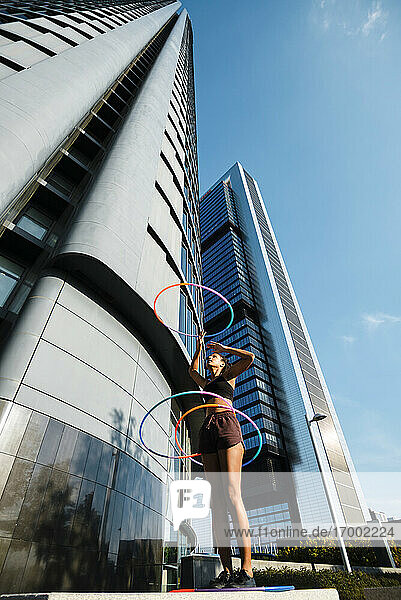 Sportliche Frau  die mit Plastikreifen vor einem Bürogebäude gegen den blauen Himmel trainiert