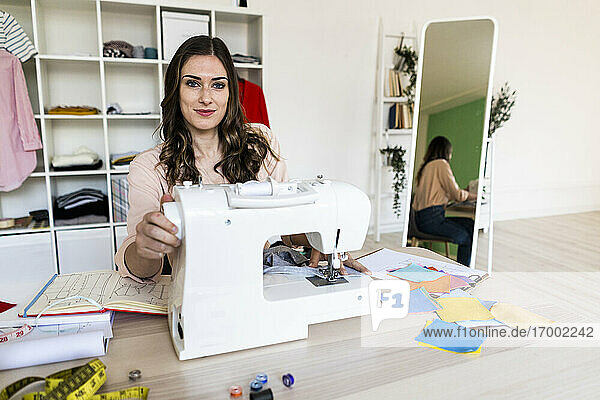 Lächelnde kreative Schneiderin  die in einem Atelier an einer Nähmaschine sitzt