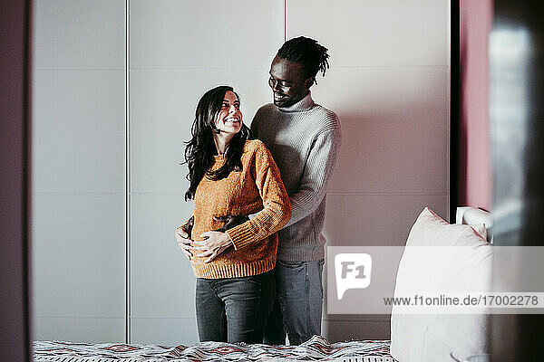 Happy man embracing pregnant woman in bedroom at home