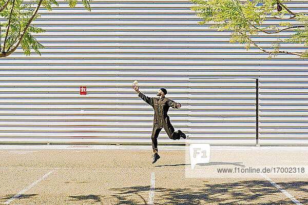 Man wearing black overall jumping in the air in front of industrial building