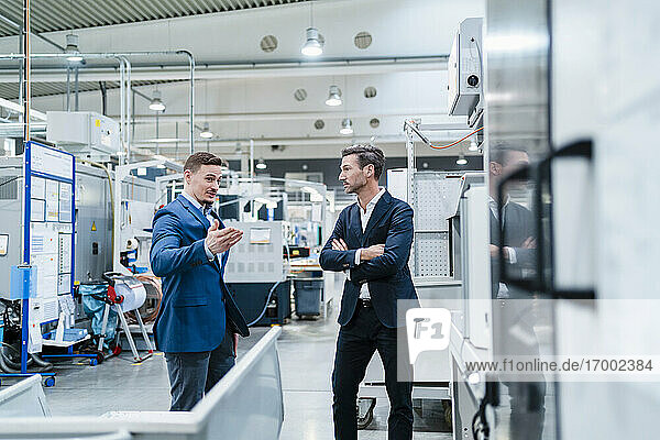 Geschäftsleute diskutieren  während sie in einer von Maschinen umgebenen Fabrik stehen
