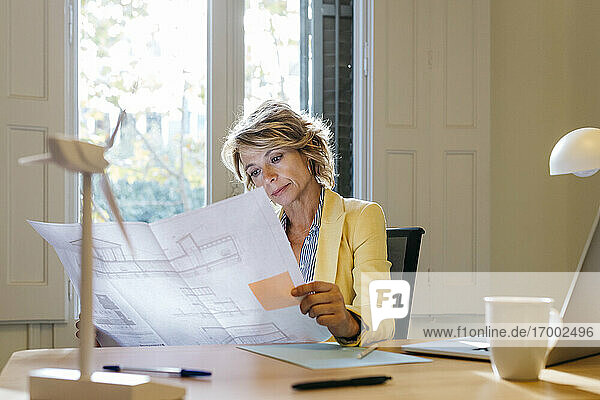 Female engineer analyzing blueprint while sitting in office