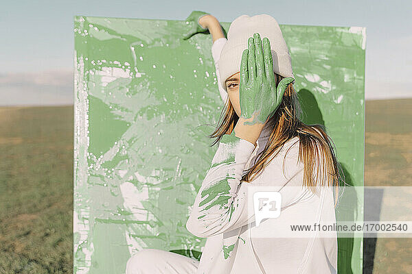 Young woman standing in front of painting  covering eye with green hand