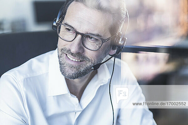 Smiling businessman wearing headphones looking away while sitting at office