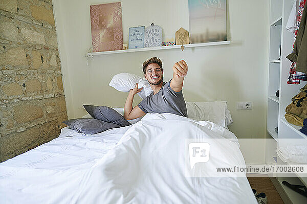 Verspielter Mann spielt mit Kissen im Schlafzimmer zu Hause